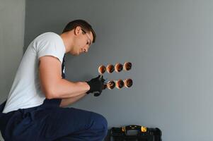 Electrician in uniform mounting electric sockets on the white wall indoors photo