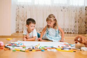 niños dibujo en piso en papel. preescolar chico y niña jugar en piso con educativo juguetes - bloques, tren, ferrocarril, avión. juguetes para preescolar y jardín de infancia. niños a hogar o guardería foto