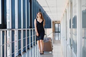 joven mujer con equipaje a el internacional aeropuerto. ella es muy contento de su vacaciones a calentar país en Navidad Días festivos foto