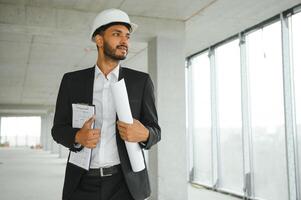 Asian engineer handsome man or architect with white safety helmet in construction site. Standing at modern building construction. Worker asian man working project building photo