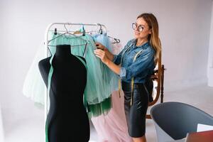 atractivo hembra Moda diseñador es trabajando en su taller. elegante mujer en proceso de creando nuevo ropa colección foto