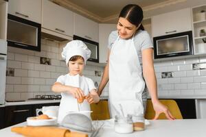 contento madre y su pequeño hijo sacudida crudo huevos en cuenco antes de haciendo masa para hecho en casa Pastelería en el cocina foto