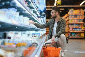 Portrait of smiling handsome man grocery shopping in supermarket, choosing food products from shelf photo