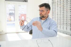 lentes controlar, mayor visión y mayor hombre a un consultante optometría clínica para bienestar. feliz, sonrisa y antiguo cara con lente, marco y gafas elección en un Tienda para ayuda consiguiendo un prescripción. foto