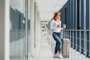 Portrait of successful business woman traveling with case at airport. Beautiful stylish female travel with luggage. Woman waiting for plane and drinking coffee photo