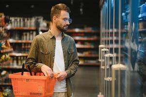 Portrait of smiling handsome man grocery shopping in supermarket, choosing food products from shelf photo