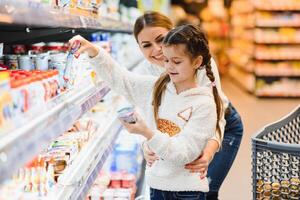 hermosa madre participación tienda de comestibles cesta con su niño caminando en supermercado. compras para saludable. foto