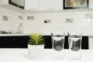 Two glasses of water in kitchen, with tap. Water shortage concept. photo