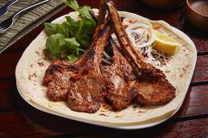 Grilled Lamb Chops with lemon, salad and bread served in dish isolated on table side view of middle east food photo