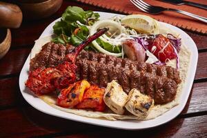 Mixed Tandoori Grills platter with tikka boti kabab, salad, lemon and bread served in dish isolated on table side view of middle east food photo