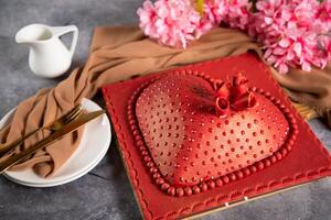 Heart Shaped red Cake with rose flowers, knife and fork served on board isolated on napkin side view of cafe baked food photo