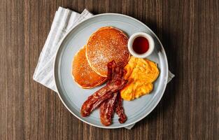 Full American Breakfast butter Pancakes fried Eggs And Bacon and sausages served on white plate on wooden table top view photo