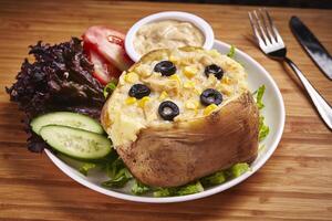 Jacket Potatoes with olive, corn, salad, cucumber, dip and tomato served in dish isolated on table side view of middle east food photo