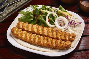 Spicy bbq lamb kabab with salad, lemon and bread served in dish isolated on table side view of middle east food photo