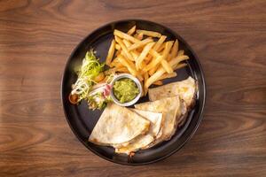 Grilled Beef Quesadilla with fries and salad served in a dish top view on dark wooden background photo