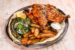 Full grilled chicken with salad, wedges, lemon and dip served in dish isolated on background top view of arabic food photo