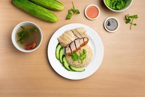 Steamed Chicken and Roast Pork Rice with raw cucumber, Coriander, salad, sauce and soup served in a dish isolated on wooden background top view photo