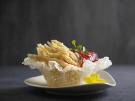 Thai Style Crispy fried Silver Bait served in a dish isolated on wooden board side view dark background photo