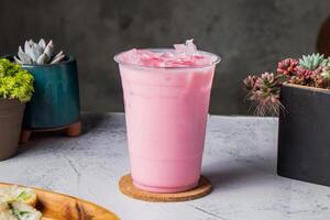 iced strawberry milk or rose milk served in disposable glass with ice cube isolated on wooden board side view of taiwanese ice drink photo