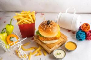 Fish Burger with fries tomato, and green chilli isolated on wooden board side view of american fast food photo