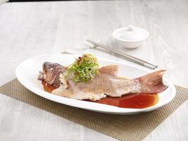 Steamed Star Grouper with Supreme Soya Sauce Served in a dish isolated on wooden board side view on grey background photo