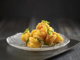 Crispy-fried Crystal Prawns with Salted Egg Yolk served in a dish isolated on cutting board side view on dark background photo