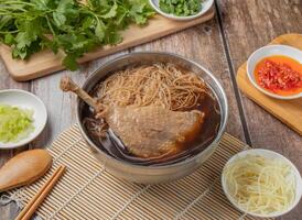 Angelica Duck Noodles Soup with chilli sauce, noodles, spoon and chopsticks served in dish isolated on napkin top view of hong kong food photo