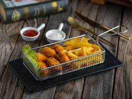 chicken nuggets with fries with ketchup and dip served in a fryer isolated on wooden background side view of appetizer photo