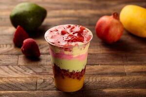 Layers cocktail of pomegranate, mango, avocado, strawberry served in glass side view on wooden table morning meal photo