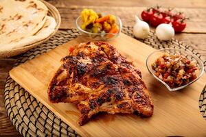 Half Grilled Chicken with bread and pickle served in a wooden cutting board isolated on wooden background side view photo