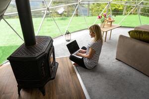 middle aged woman uses a laptop resting and spending time at Glamping house on holidays. holiday dome tent. Cozy, camping, hygge, lifestyle concept photo