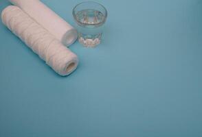 Water filters. Carbon cartridges and a glass on a blue background. Household filtration system. photo