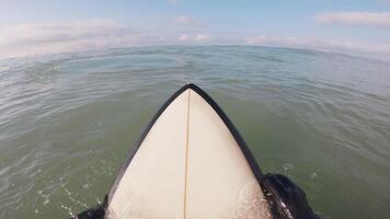 Surfer on surfboard in ocean and looking at waves with morning sunlight. First-person view of surfing in ocean video