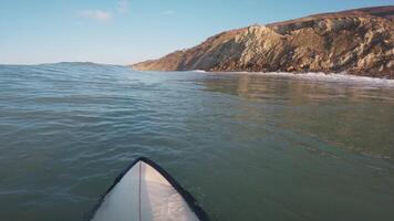 surfer Aan surfboard in oceaan en op zoek Bij golven met ochtend- zonlicht. eerste persoon visie van surfing in oceaan video