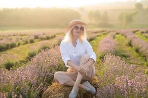 Young blond woman traveller wearing straw hat in lavender field surrounded with lavender flowers. photo