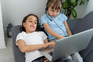 niños recibir educación a hogar en un salón de clases con un computadora portátil, en línea cursos para niños, niño desarrollo, dos caucásico muchachas tener divertido y reloj caricaturas, educación en el hogar foto