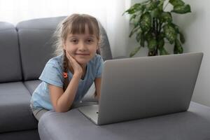 pequeño niña estudiando con computadora, pequeño niña con ordenador portátil en línea. foto