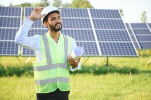 Male arab engineer standing on field with rows of solar panels. photo