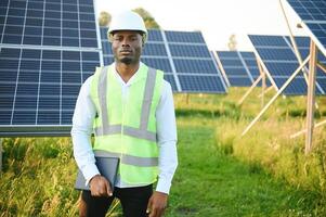 Close up portrait of young handsome African American craftsman a protective helmet. Happy man in overalls posing at camera smiling. Slow motion. photo