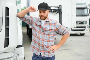 Portrait of young Caucasian bearded trucker standing by his truck vehicle. Transportation service. Truck driver job. photo