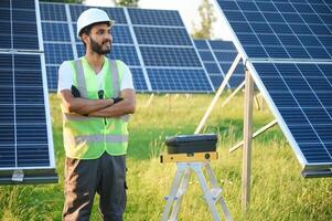 Male arab engineer standing on field with rows of solar panels. photo