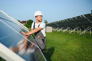 Side view of male worker installing solar modules and support structures of photovoltaic solar array. Electrician wearing safety helmet while working with solar panel. Concept of sun energy photo