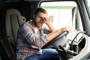 Tired of work. Sitting in the cabin. Young truck driver is with his vehicle at daytime. photo