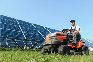 A man drives a lawnmower near solar panels. Concept of solar energy photo