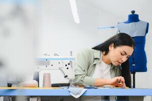 Young dressmaker woman sews clothes on working table. Smiling seamstress and her hand close up in workshop. photo