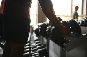 Hot african american young man bodybuilder lifting barbell at gym, working on his arms, looking at copy space. Black muscular shirtless guy having biceps workout session. Healthy lifestyle concept. photo