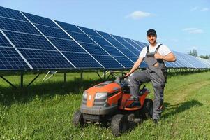 A man working at solar power station. A worker on a garden tractor mows grass on a solar panel farm. photo