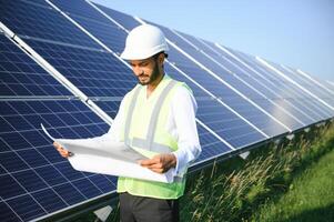 Male arab engineer standing on field with rows of solar panels. photo