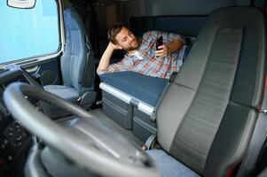un camionero en el taxi, acostado en el camión cama, desplazamiento en su teléfono durante su de repuesto tiempo. foto