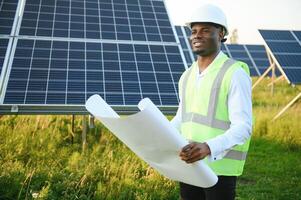 Close up portrait of young african american engineer worker in hardhat holding solar plan. Green electricity future concept. photo